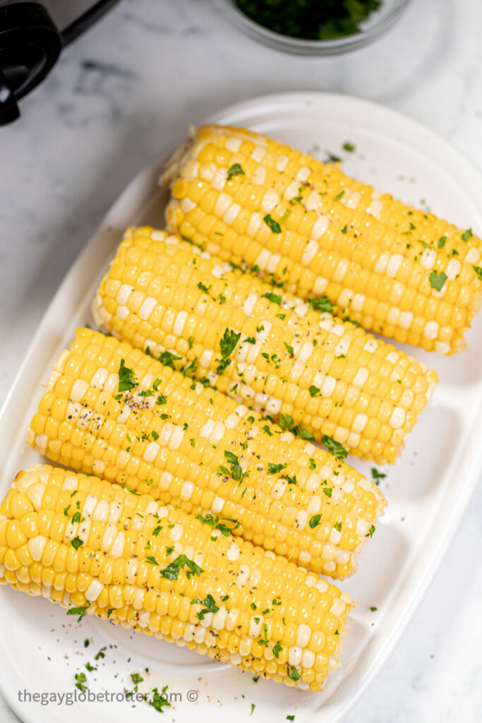 Corn in the cob on a platter garnished with parsley and butter.