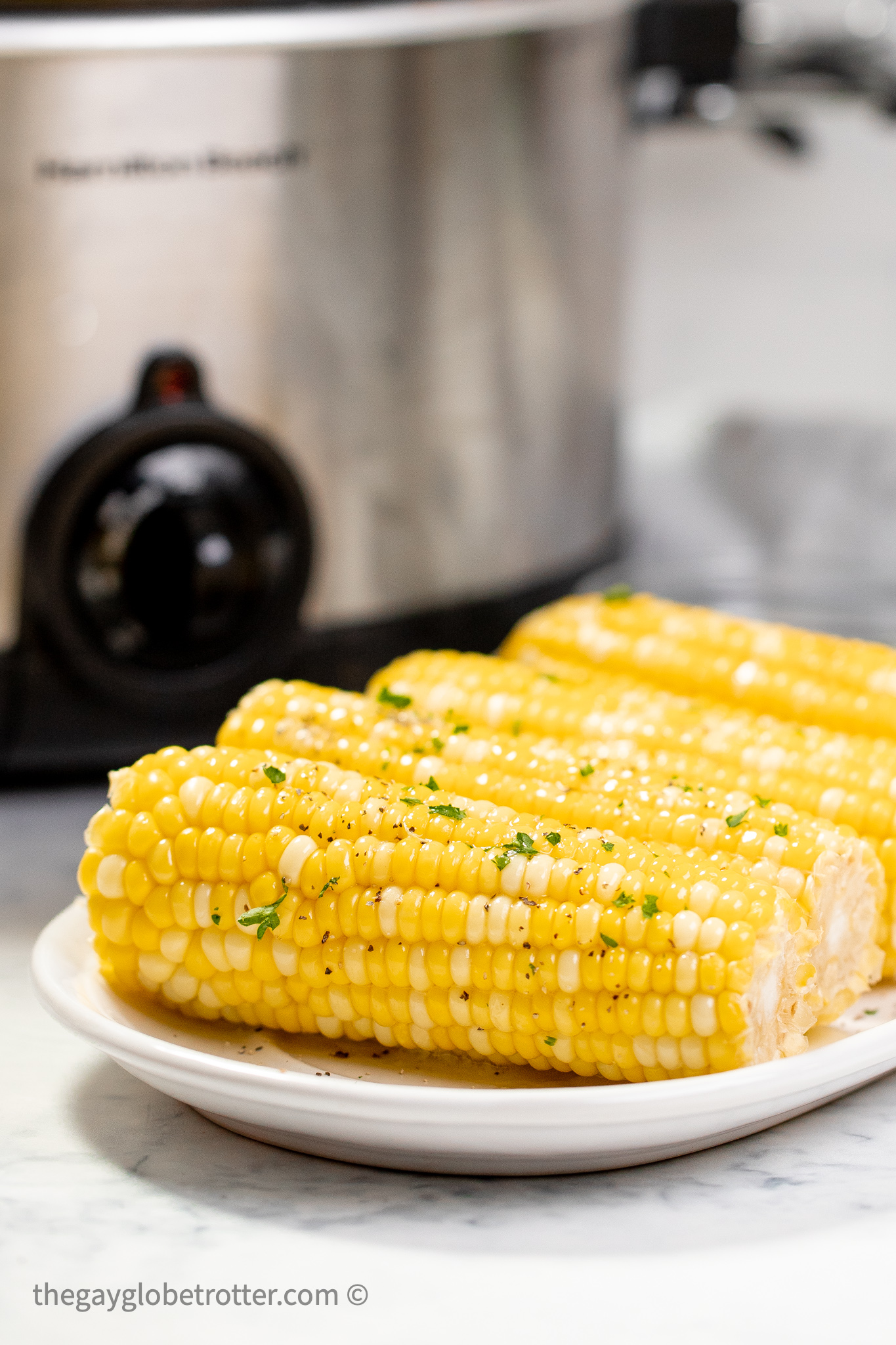 Corn on the cob on a platter next to a CrockPot.