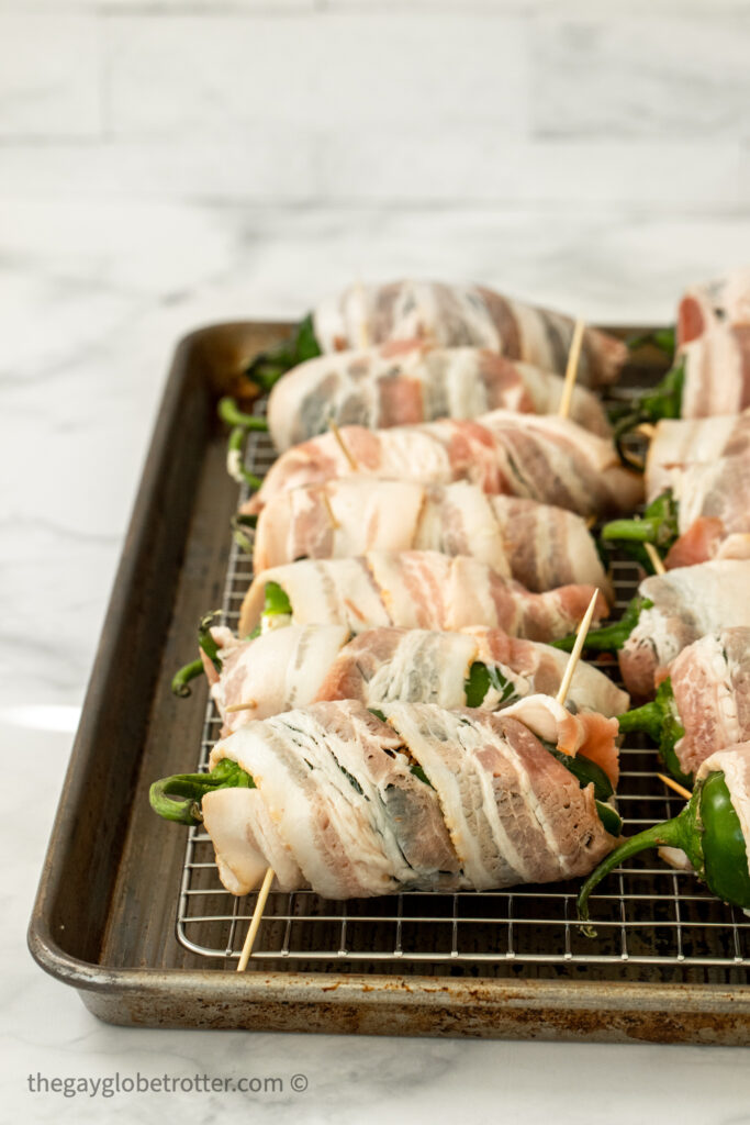 Jalapenos wrapped in bacon on a baking sheet.