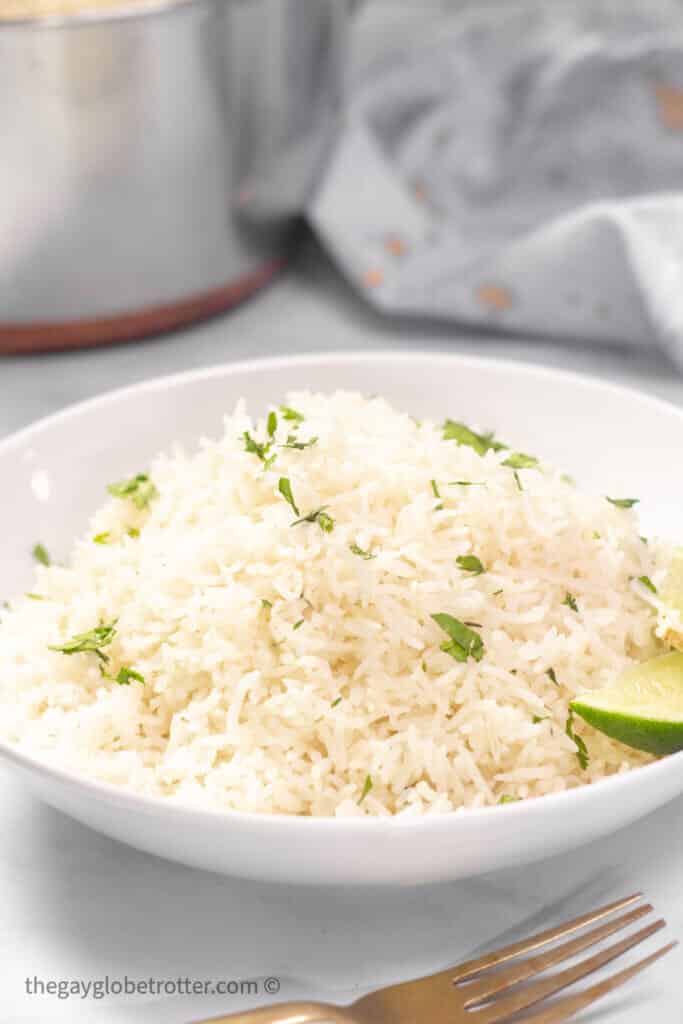 A bowl of coconut rice with limes and cilantro.