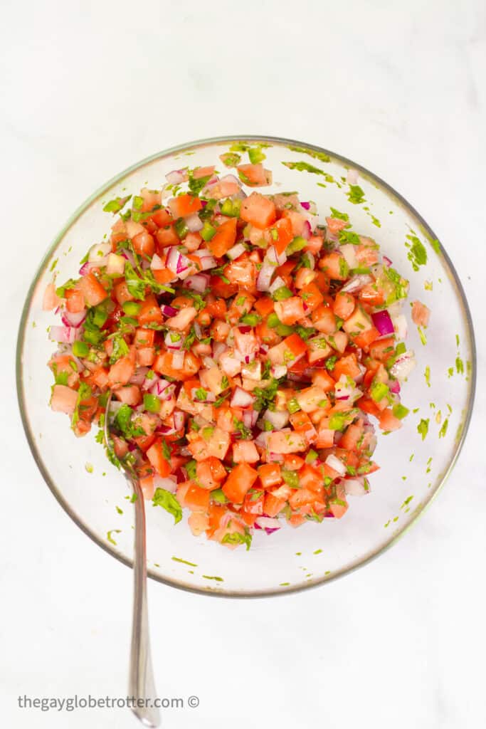 Pico de gallo in a mixing bowl with a spoon.