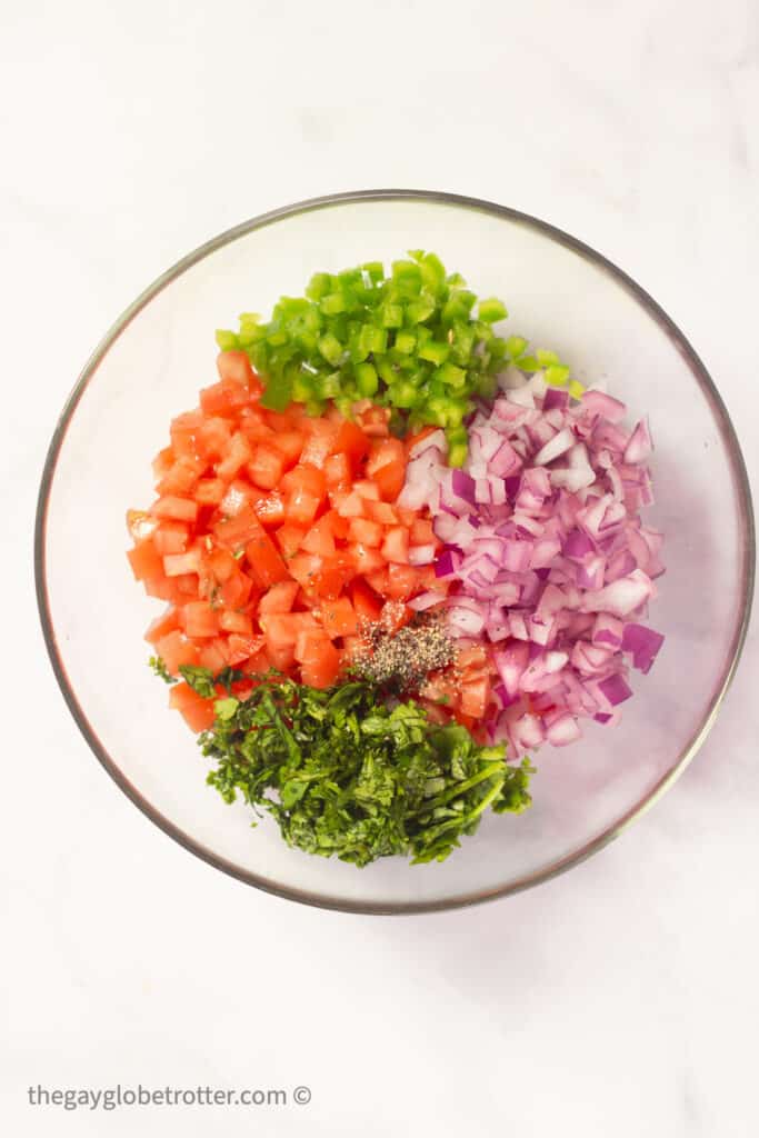 Tomatoes, red onions, jalapenos, and cilantro in a clear bowl.