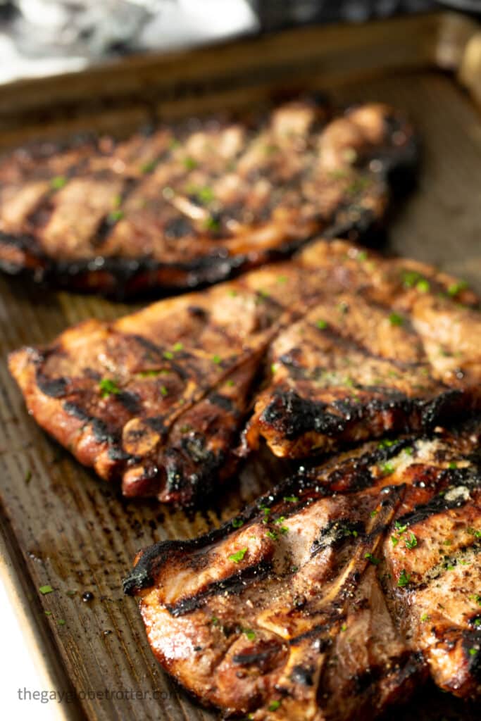 Grilled pork shoulder steaks garnished with parsley on a baking sheet.