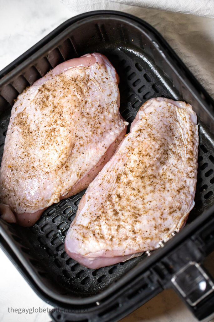 Raw turkey breast in an air fryer basket with seasonings.
