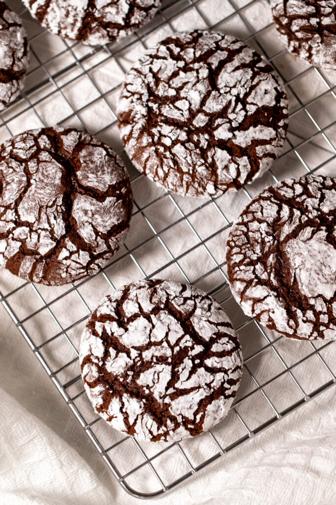 A batch of chocolate crinkle cookies on a cooling rack.
