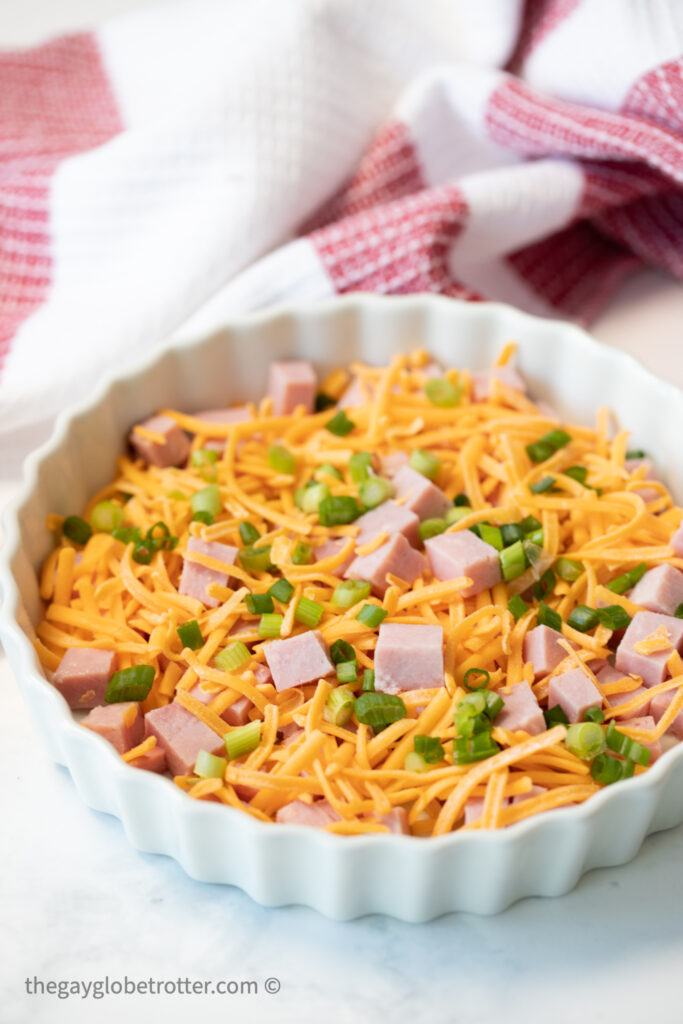 Ham, cheese, and green onions in a pie dish.