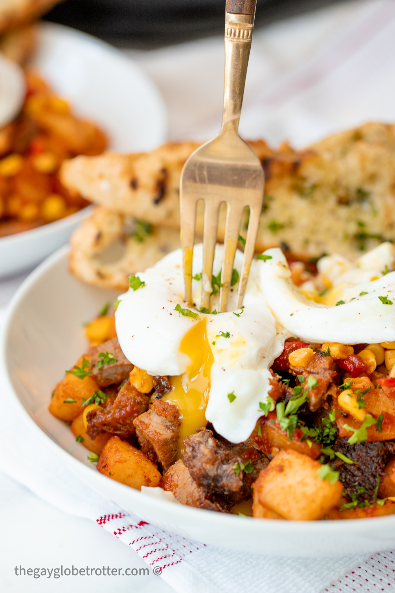 A fork breaking a poached egg on roast beef hash.