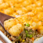 A serving spoon scooping tater tot casserole.