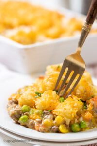 A fork digging into tater tot casserole on a plate.