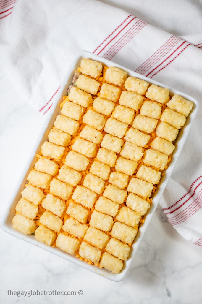 Frozen tater tots arranged on a beef and vegetable layer.