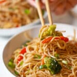 Chopsticks picking up vegetable chow mein from a bowl.