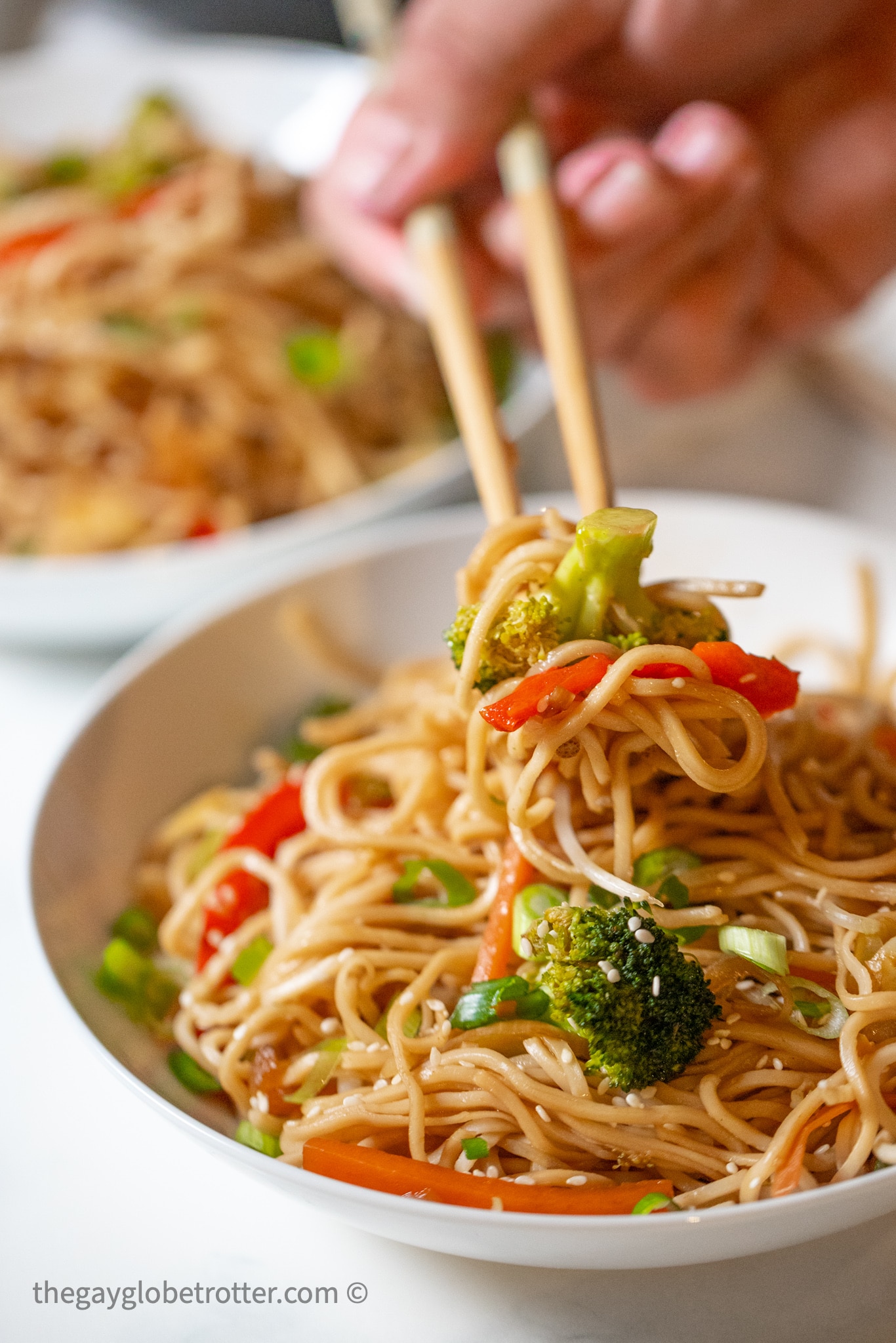 Chopsticks picking up vegetable chow mein from a bowl.