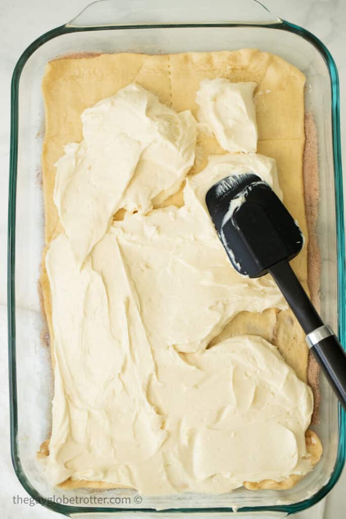 A spatula spreading cheesecake filling on crescent roll dough.