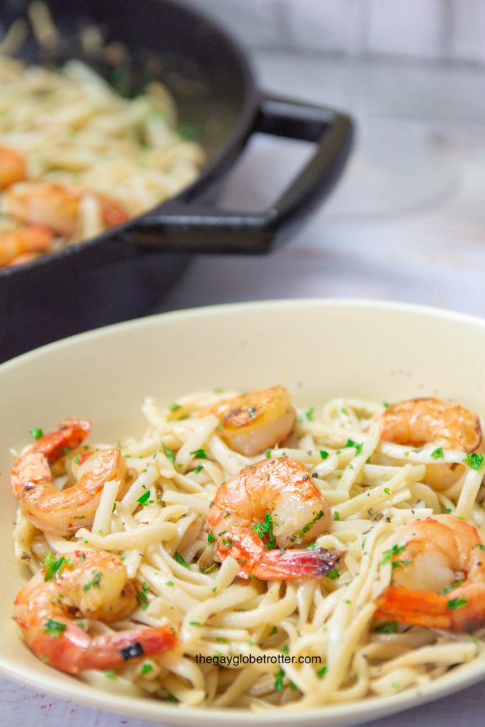 A bowl of shrimp scampi with pasta next to a pan with more shrimp scampi.