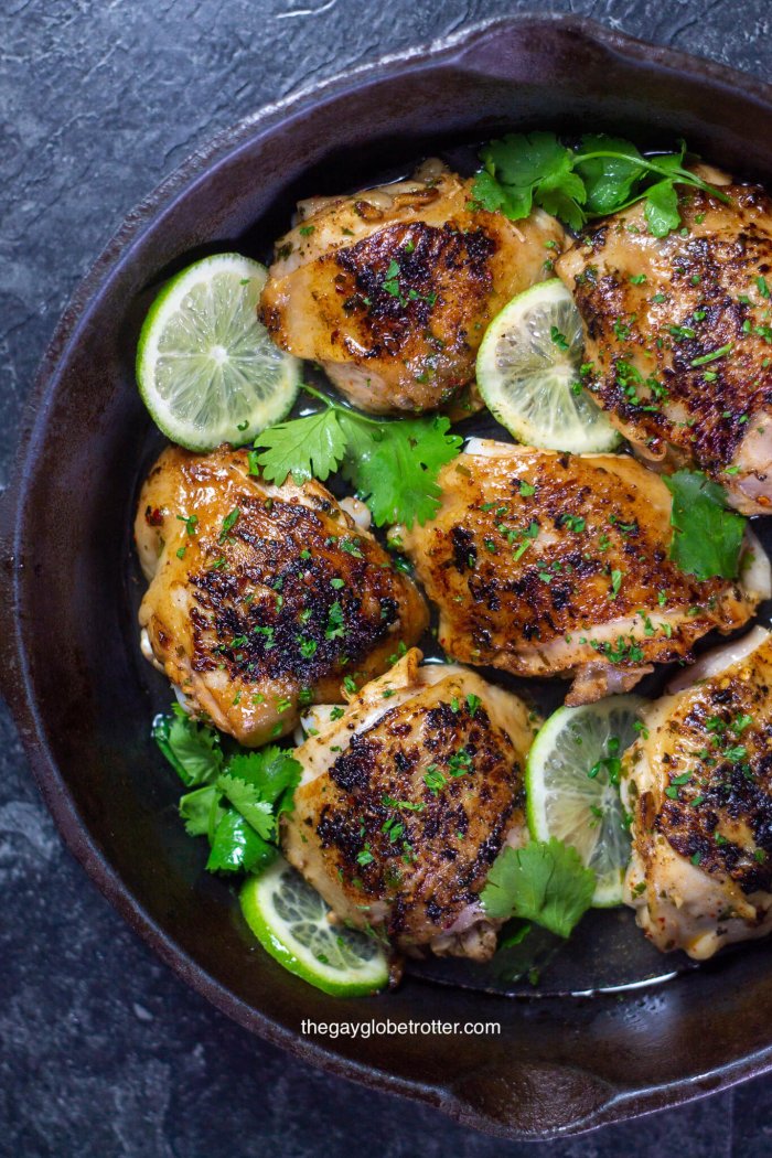 An overhead shot of cilantro lime chicken in a cast iron pan surrounded by fresh limes and cilantro.