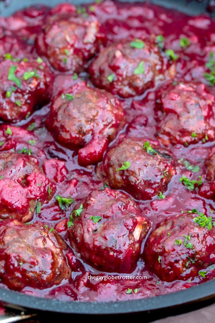 Savoury cranberry meatballs in a sauce pan topped with fresh parsley.