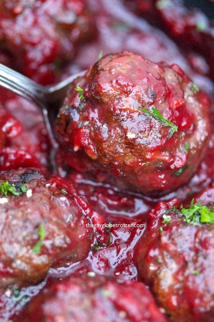 Savoury cranberry meatball getting served on a silver spoon.