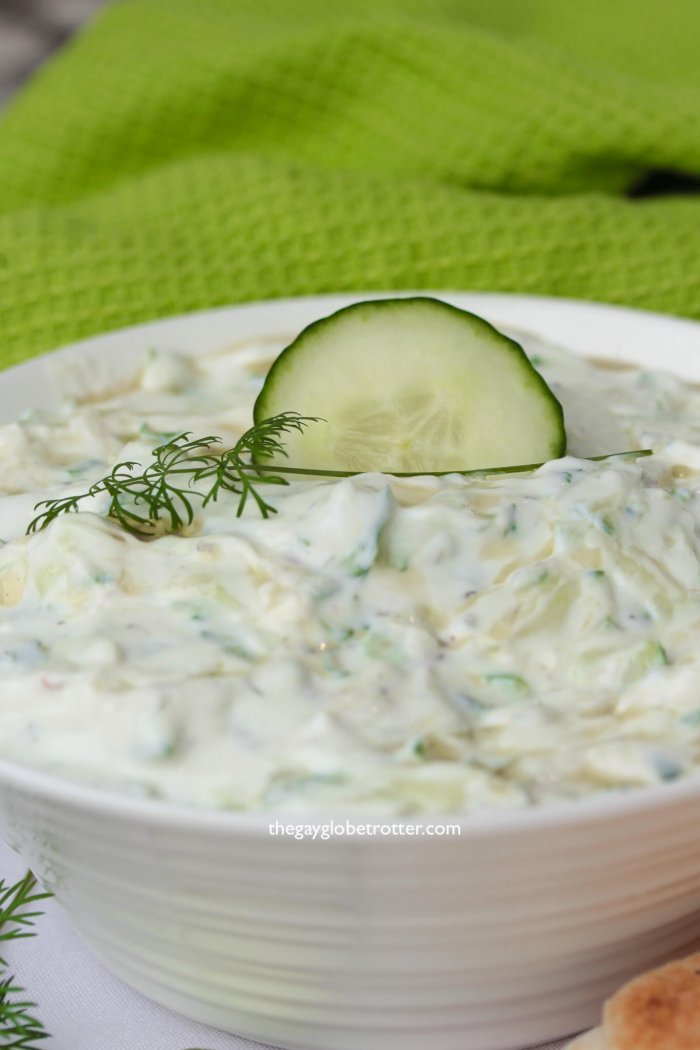 A bowl of tzatziki sauce with dill and a fresh cucumber