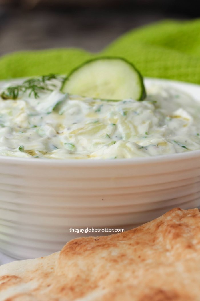 A bowl of homemade tzatziki with pita and cucumbers.